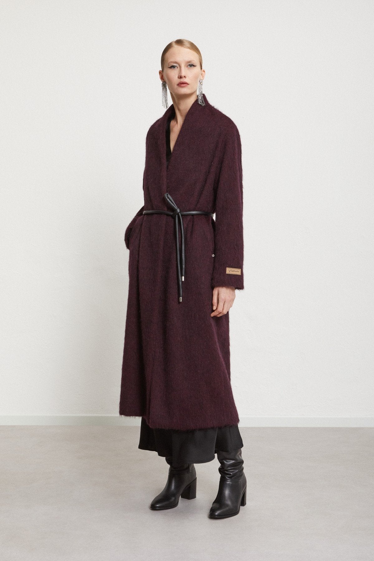 Model styling the belted burgundy coat with black ankle boots.