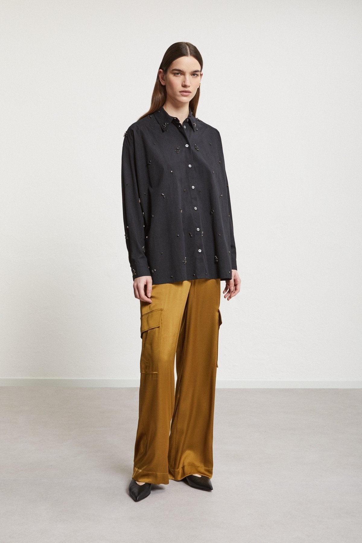 Front view of a model wearing Ottod’Ame bronze-gold trousers with a black shirt.