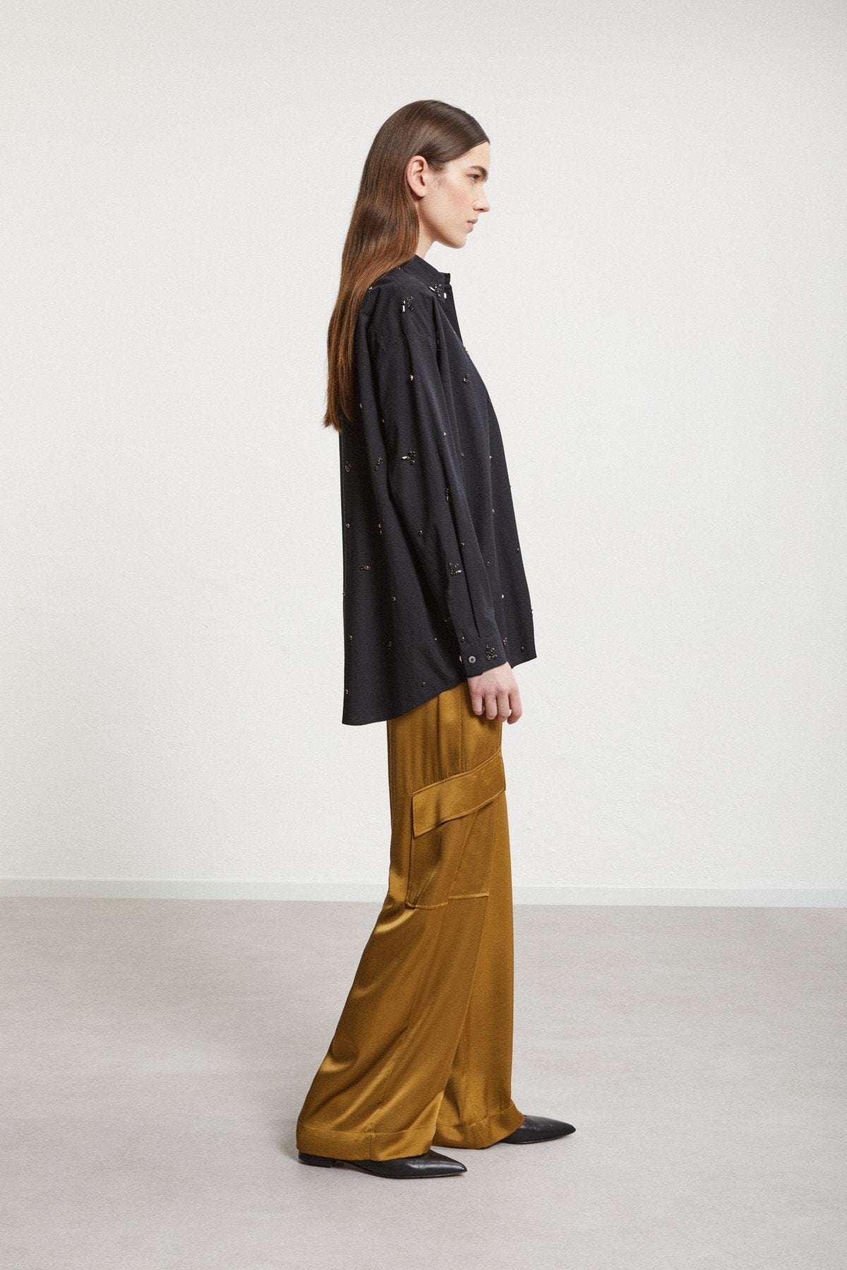 Side view of a model wearing bronze-gold wide-leg trousers with a black embellished jacket.