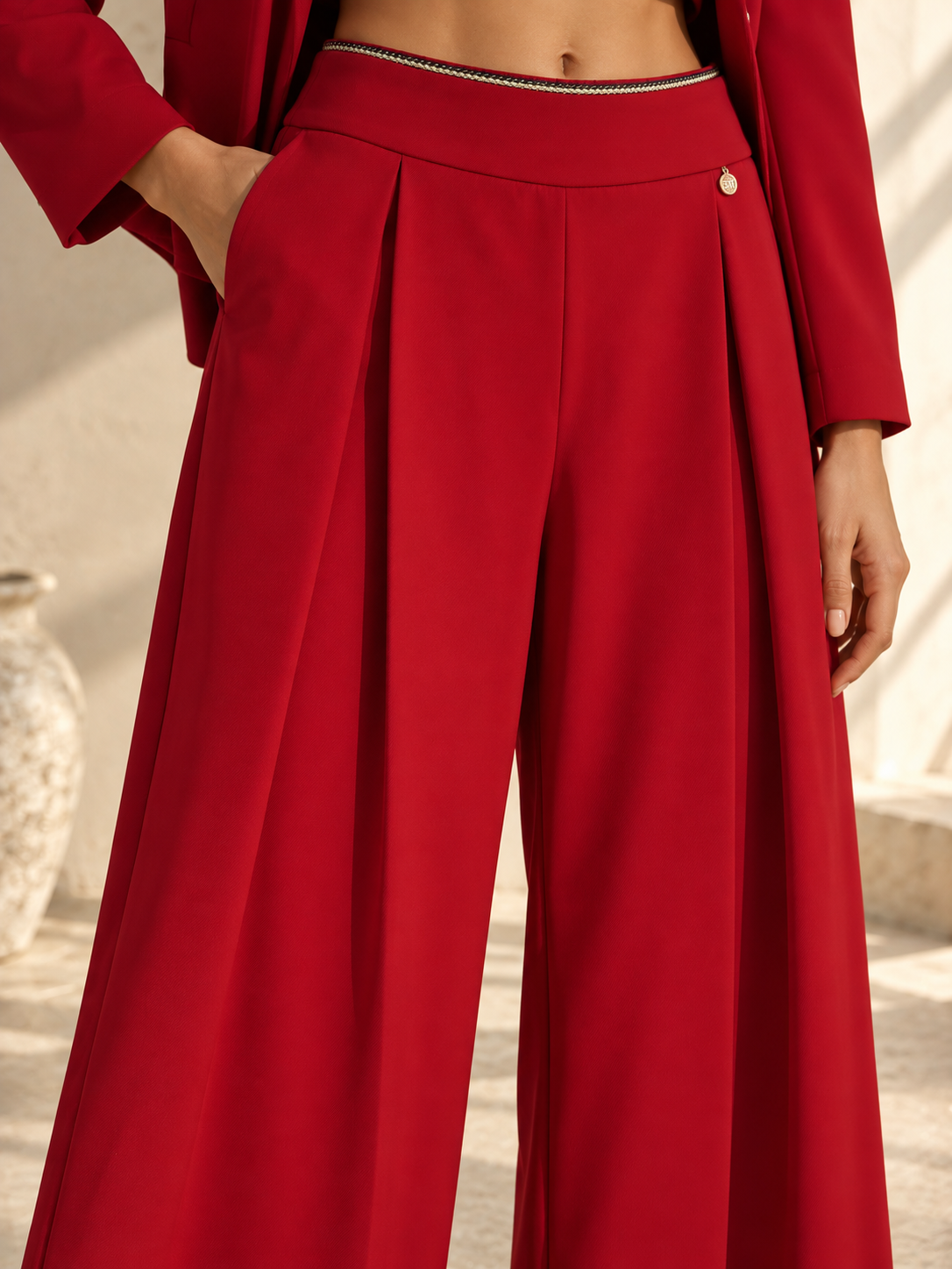 Close-up of red trousers showing gold chain waistband and signature charm
